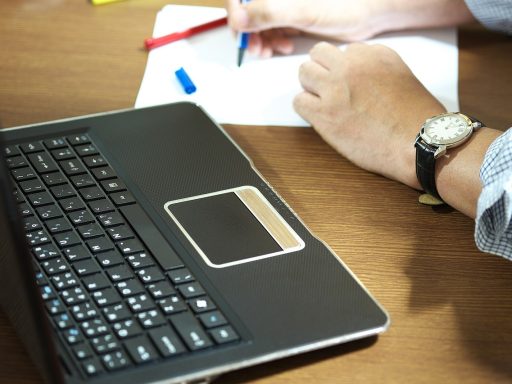 Persoon die achter een laptop studeert aan een bureau, bezig met een online cursus of opleiding